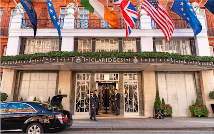 The grand entrance of Claridge's, one of the renowned boutique hotels in London, is shown with flags and waiting doormen.