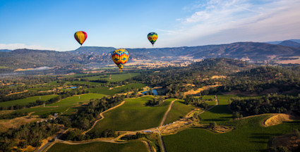 Aerial view of Napa Valley during the summer with several hot air balloons in the air.