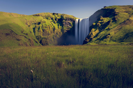 Image of a waterfall in the distance surrounded by lush greenery.