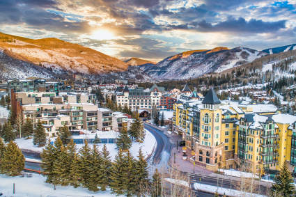The snowy alpine trails of one of the best ski towns in the country sit in the distance as sunlight hits the buildings. 