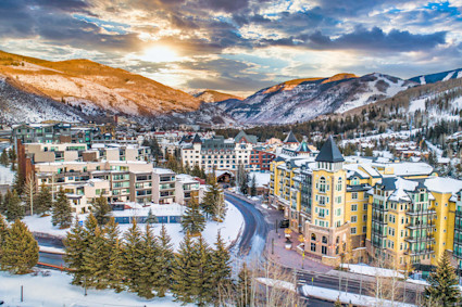 The snowy alpine trails of one of the best ski towns in the country sit in the distance as sunlight hits the buildings.