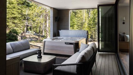 A serene covered deck of an Olympic Valley second home with a hot tub and comfortable seating surrounded by wooded forests.