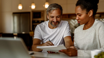 Two people calculate their down payment using a laptop, pen and paper.
