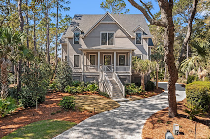 Coastal-style Kiawah Island home with shingled gables, wraparound porch, and a winding paver driveway through the trees.