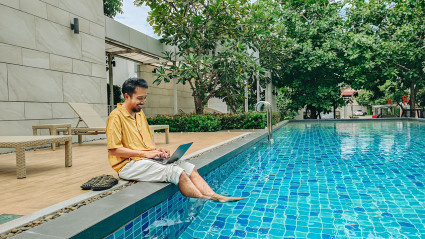 A person researches Plum Guide alternatives on their laptop while sitting by a pool.