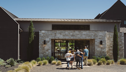 A family arm-in-arm walking into the front door of a luxury home with lots of planted shrubs around the exterior.