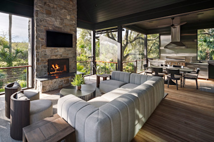 Screened outdoor living space with stone fireplace, TV, sectional seating, dining area, and fully equipped outdoor kitchen.