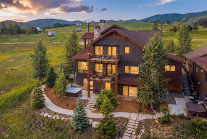 Three-story mountain home glowing at dusk, framed by aspens and rolling ski slopes with gondolas overhead.