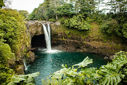 A waterfall flows into a cove surrounded by lush greenery.