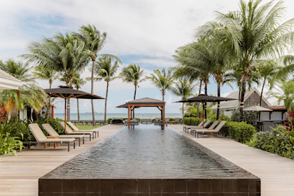 Infinity pool with dark tile edge, wood deck, lounge chairs, and ocean view framed by palms
