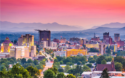 Asheville’s skyline and the Blue Ridge Mountains light up at dusk, securing its spot as one of the most beautiful places in the US.