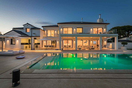 White luxury villa within Infinity by Pacaso with lit outdoor pool at night in Marbella, Spain.