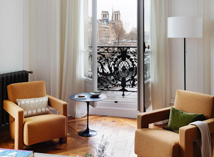 Elegant Parisian sitting room with herringbone floors, ornate iron balcony, and Notre-Dame Cathedral visible through the window.