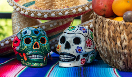 Colorful sugar skills on a table with a basket of fruit and a sombrero.