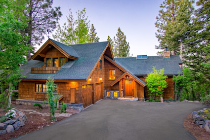 Exterior of Pine View with wood siding and large pine trees surrounding the home with a paved driveway.