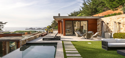 Modern coastal retreat at golden hour with infinity pool, sun loungers, and a stone patio overlooking the Pacific Ocean.