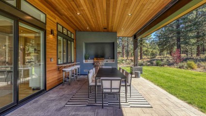 Covered outdoor patio with a large dining table, built-in grill and woodland views