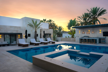 Solana outdoor lounge area with cushioned chairs surrounding the fire pit with a rectangular pool and hot tub.