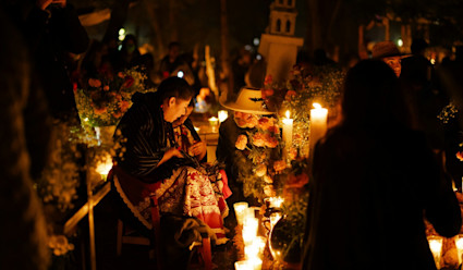 Family visiting a cemetery at night surrounded by candles and flowers.