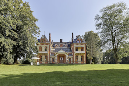 Historic estate exterior with ornate brick facade, twin gabled towers and expansive green lawn surrounded by mature trees