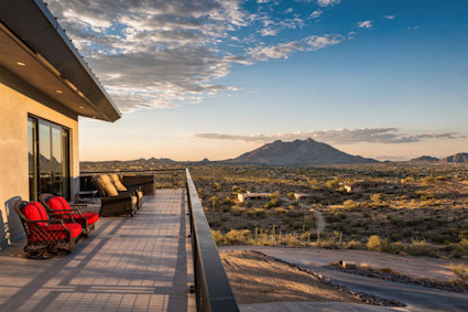 Desert terrace with red-cushioned chairs overlooking saguaro-dotted valley and a distant mountain at sunset.