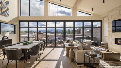 An open plan living area of a Jackson second home with floor-to-ceiling windows, natural lighting, decorative art and a relaxing area for gathering around the fireplace and dining table