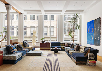 Open-plan living room with coffered ceiling, modular sofas, white marble fireplace and large windows overlooking city