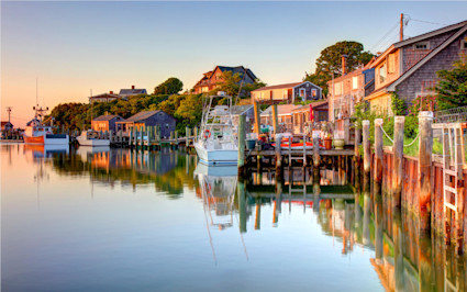 Fishing shacks and sailboats glow in a harbor at sunset, making Martha’s Vineyard one of the most beautiful places in the US.
