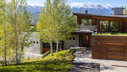 Exterior view of Jackson home with a living roof, green aspen trees in the front yard, and the Tetons looming in the distance.