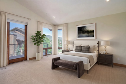 Bright primary bedroom with king bed, plaid pillows, and floor-to-ceiling glass doors opening to a private balcony with mountain views.