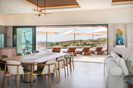 Living area with large wooden table that seats ten with a sliding wall that leads out to pool and outdoor lounge area.