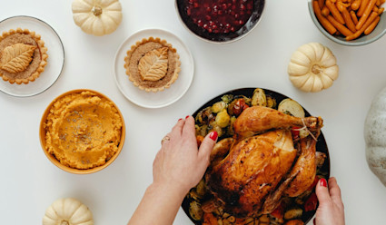 Thanksgiving turkey being placed on table alongside side dishes, pies, and decorative pumpkins.