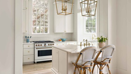  White kitchen with a gold pendant light hanging above and rattan bar chairs