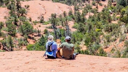A couple rests with their dog at Sedona while taking in the beautiful red scenery, a great attraction for pet-friendly vacations.