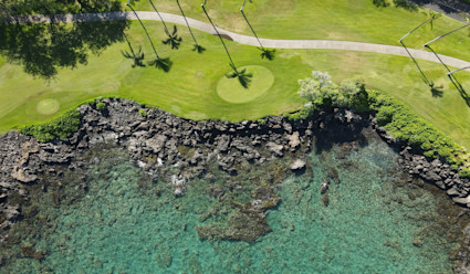 A golf course along a a shoreline of lava rock and turquoise water.