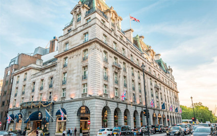The Ritz London, one of the famous London hotels, sits on a bustling street with cars and pedestrians.