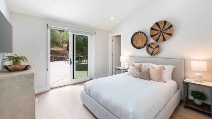 A guest bedroom of a Napa second home featuring a white bed and sliding glass doors, offering a serene ambiance and ample natural light