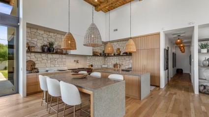 A modern kitchen of a Scottsdale second home with warm limestone backsplash, two islands, open wood shelving, and Sub-Zero and Wolf appliances