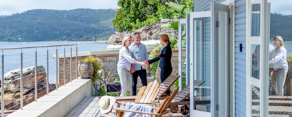 A couple meets with a real estate agent at a lake house to learn how to buy a house in another state.