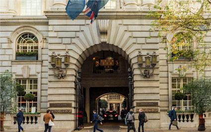People walk along the sidewalk in front of the grand arched entrance of Rosewood London, a luxury hotel in London.
