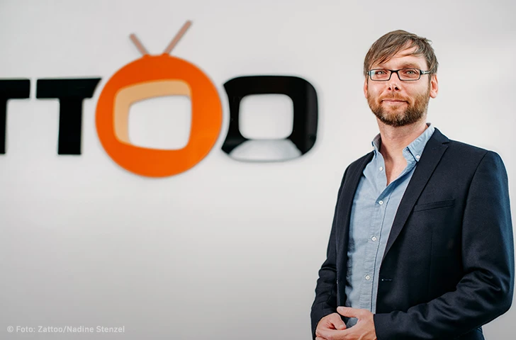 Photo Jörg Meyer Chief Commercial Officer de Zattoo debout devant le logo de la société