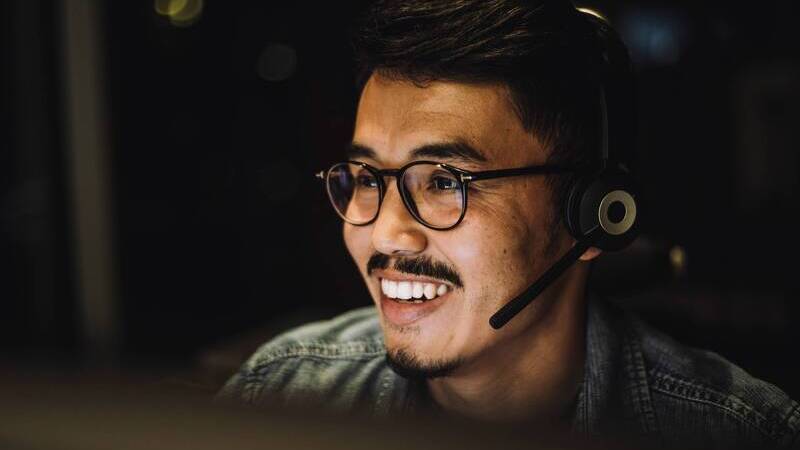 Närbild på en man som sitter framför dator med headset och glasögon.