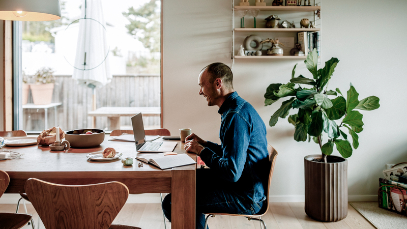 En man sitter vid ett köksbord med en laptop.