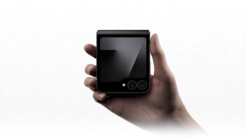 En hand håller en svart hopvikt Samsung Galaxy Z Flip7 FE med dubbla kameror och blank skärm mot vit bakgrund.