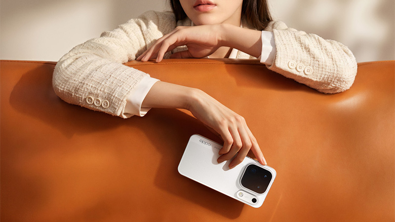 En kvinna i beige tweedkavaj lutar sig över ett brunt läderunderlag och rör vid en vit OPPO-smartphone.