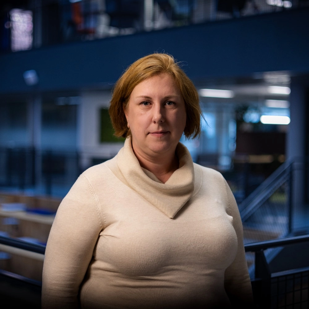 Eva Ekengren, chef över NOC (nätverksövervakning) på Tele2. Hon är klädd i en beige polotröja och har rödlätt hår. I bakgrunden syns ett kontorslandskap med öppna ytor och blå och grå färgtoner.