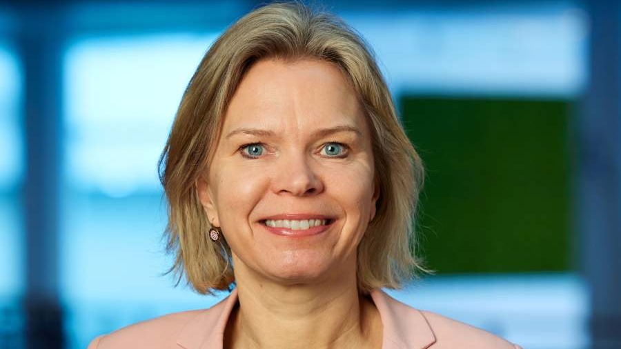 Malin Anglert, Director Customer Operations på Tele2. Hon har ljust axellångt hår och är klädd i en rosa kavaj och svart linne. Hon ler och bakom henne syns ett kontorslandskap i blå toner.