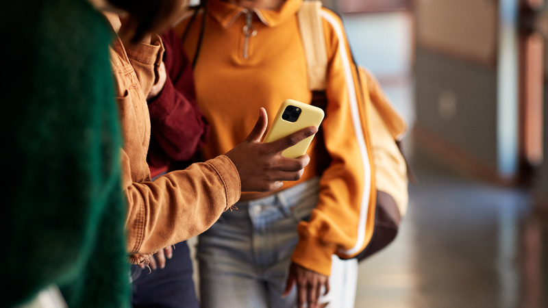 Kapad bild av ungdomar i en skolbyggnad som tittar på en mobiltelefon.