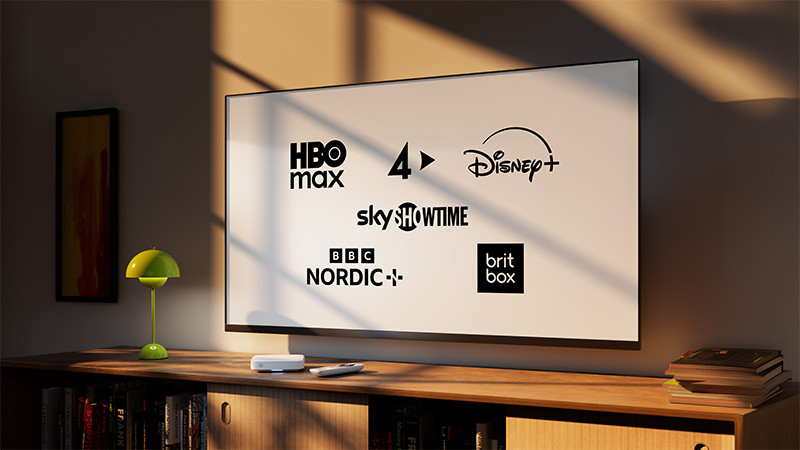 En TV på väggen visar logotyper för HBO Max, TV4, Disney+, SkyShowtime, BBC Nordic och BritBox i ett hemmarum.