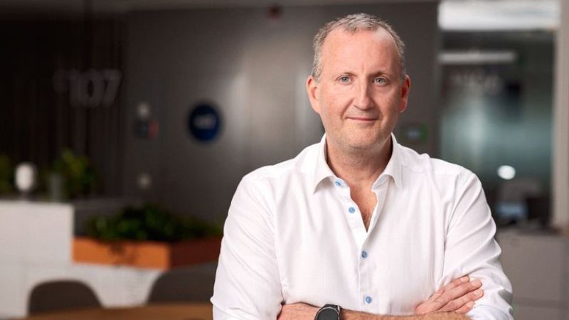 Björn Lindberg, Head Mobile Radio på Tele2. Han är klädd i vit skjorta med uppkavlade ärmar och har en svart smartklocka på vänster handled. Bakom honom syns ett kontor med mörkbruna väggar och vita skåp samt ett runt konferensbord.
